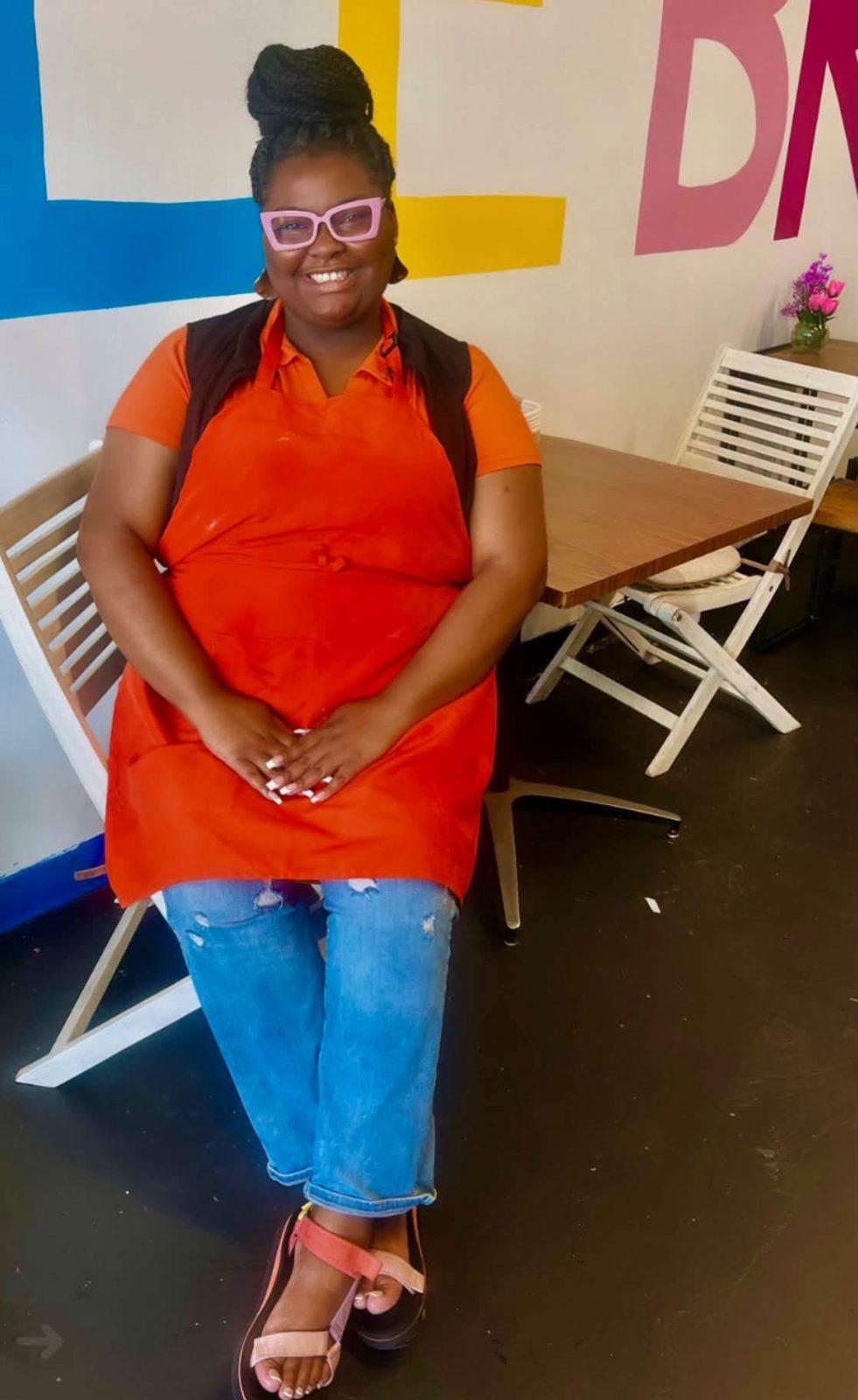 Kofee Broz team member in an orange apron in front of the letter mural