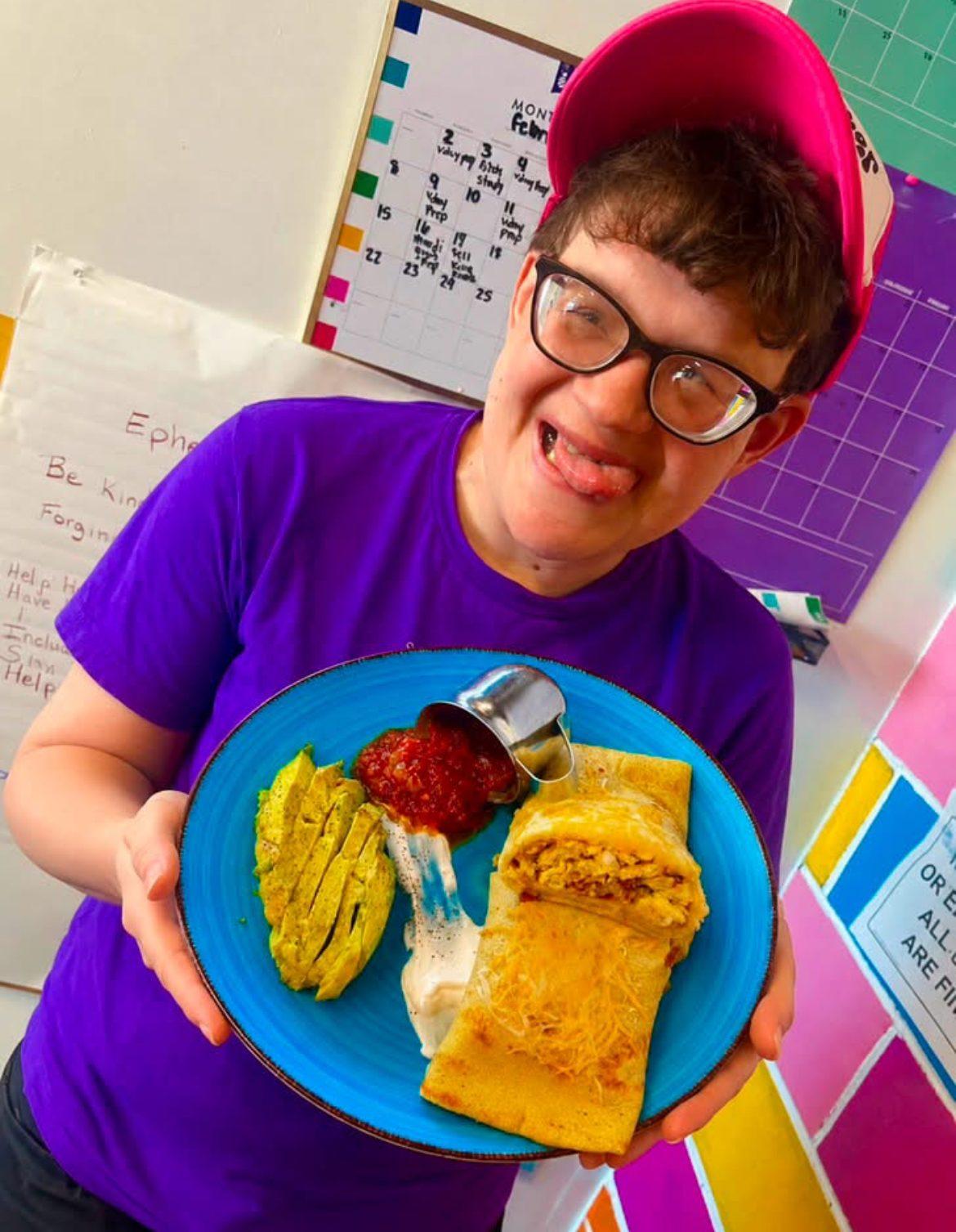 Kofee Broz team member in a pink cap proudly presenting a breakfast crepe plate