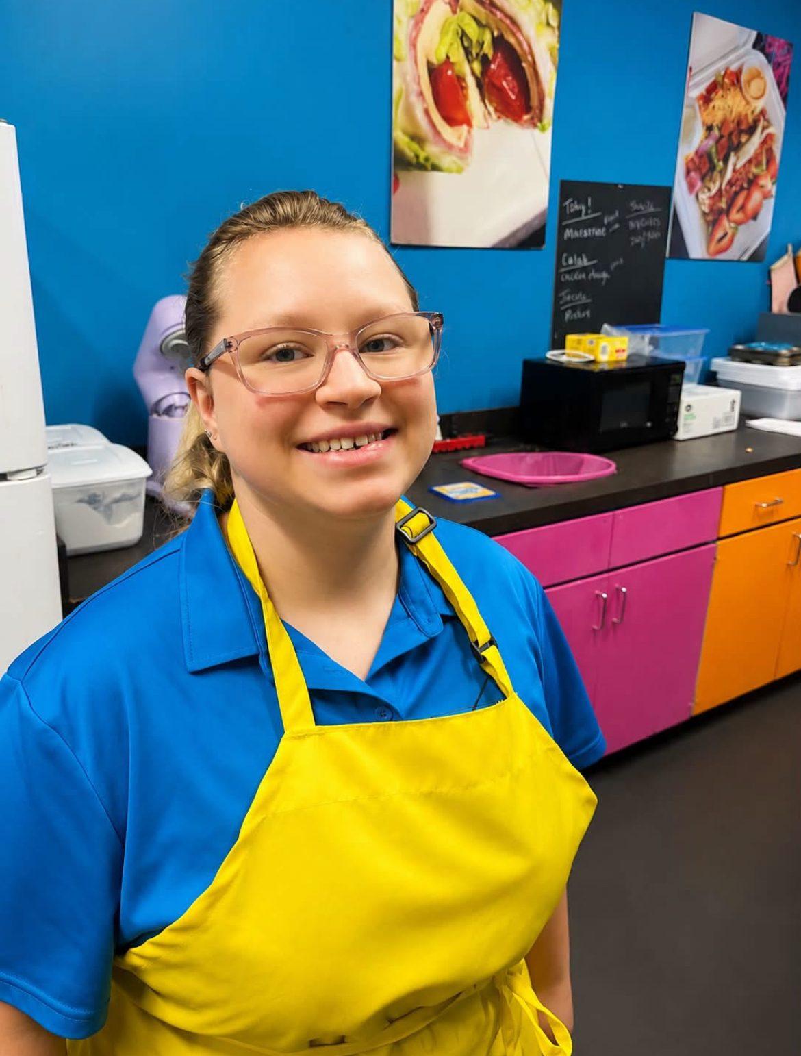 Kofee Broz barista in a yellow apron smiling behind the counter